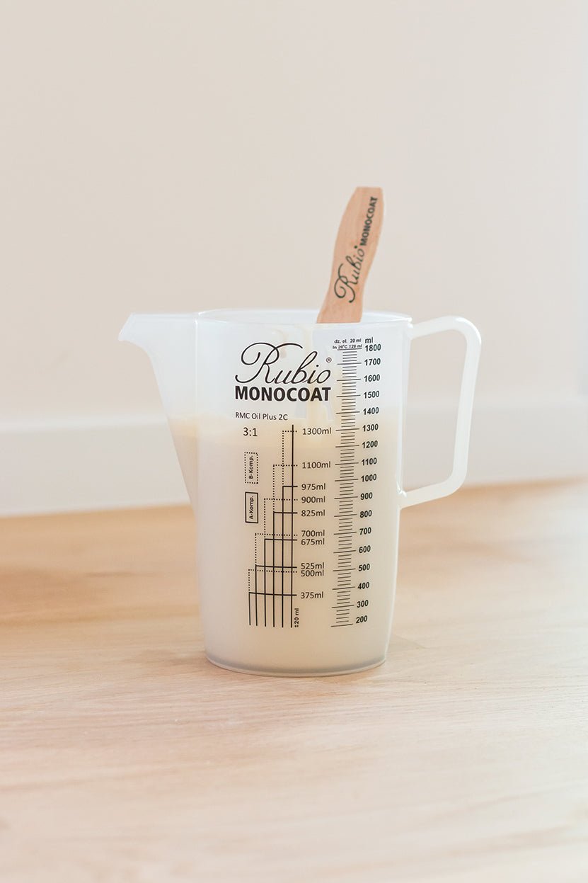 Measuring cup with a wooden stirrer on a wooden surface.