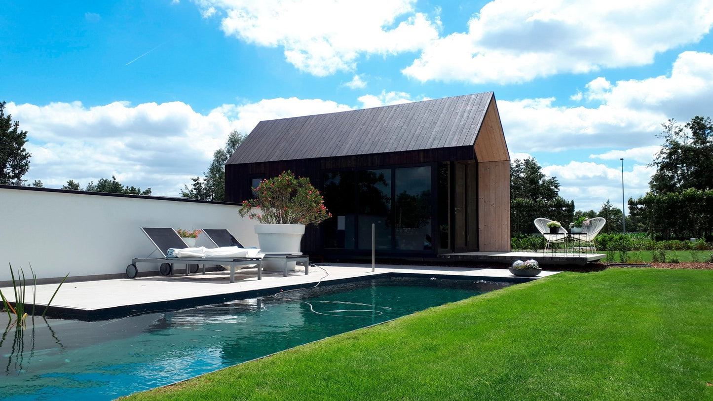 Modern poolhouse with a pool and outdoor furniture under a blue sky.